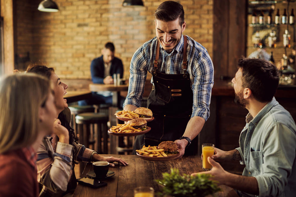 garcom-feliz-servindo-comida-para-um-grupo-de-amigos-alegres-em-um-pub